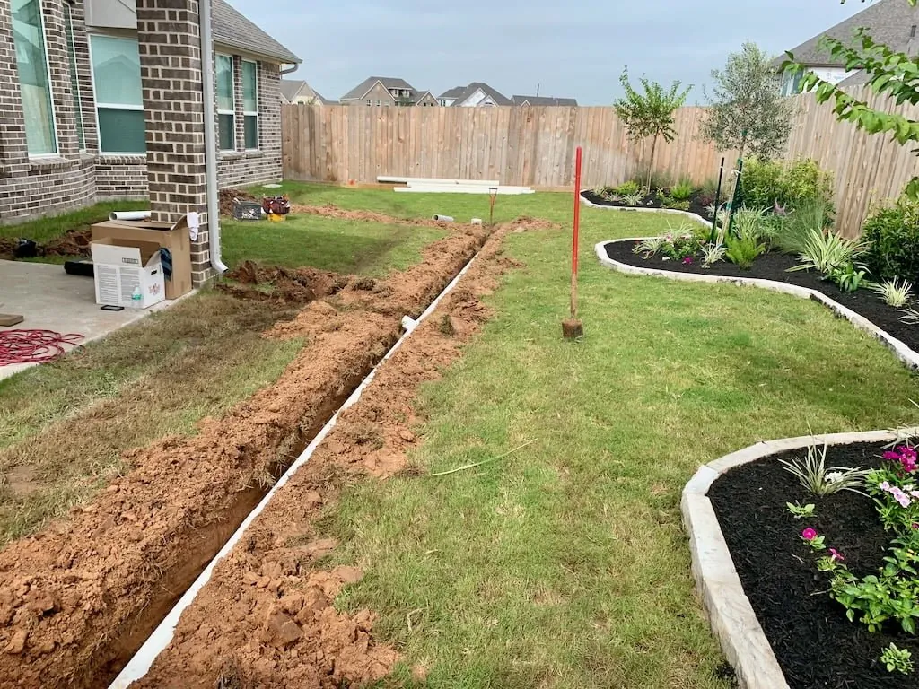 French drain trench cut across a backyard on a string line
